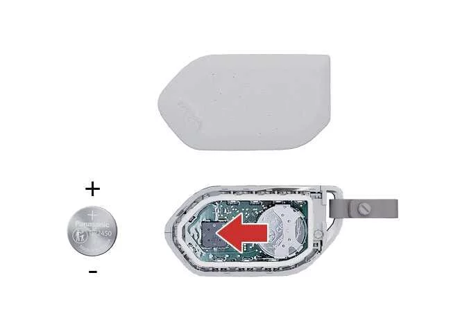 Kia K4 proximity transmitter detailing the removal of the old lithium coin cell battery from its internal retention clips and showing the correct positive orientation for the replacement cell