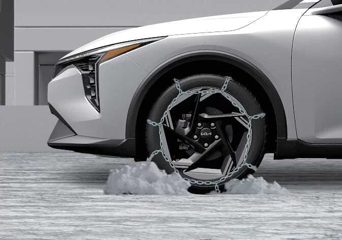 Close-up view of wire-type snow chains installed on a Kia K4 tire